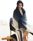 Ink Black White Ombre Textured Throw  In Hand Spun Merino And Hand Stitched Hem wrapped around a woman sitting.