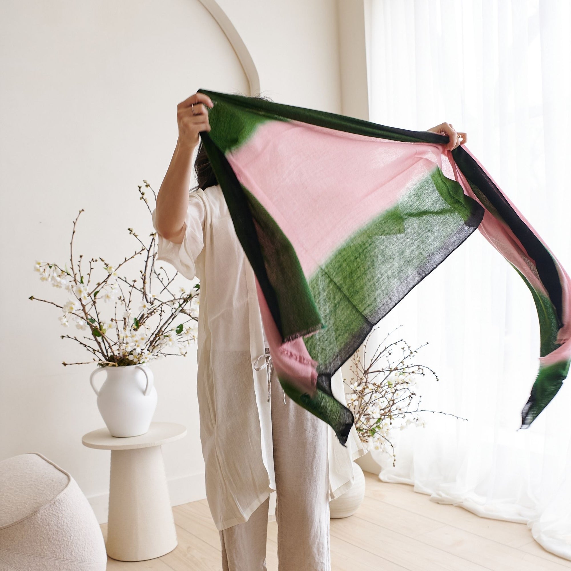 Iris Kiwi Green Pink Cashmere Merino Handwoven Scarf displayed by a model in a bright room with floral decor.