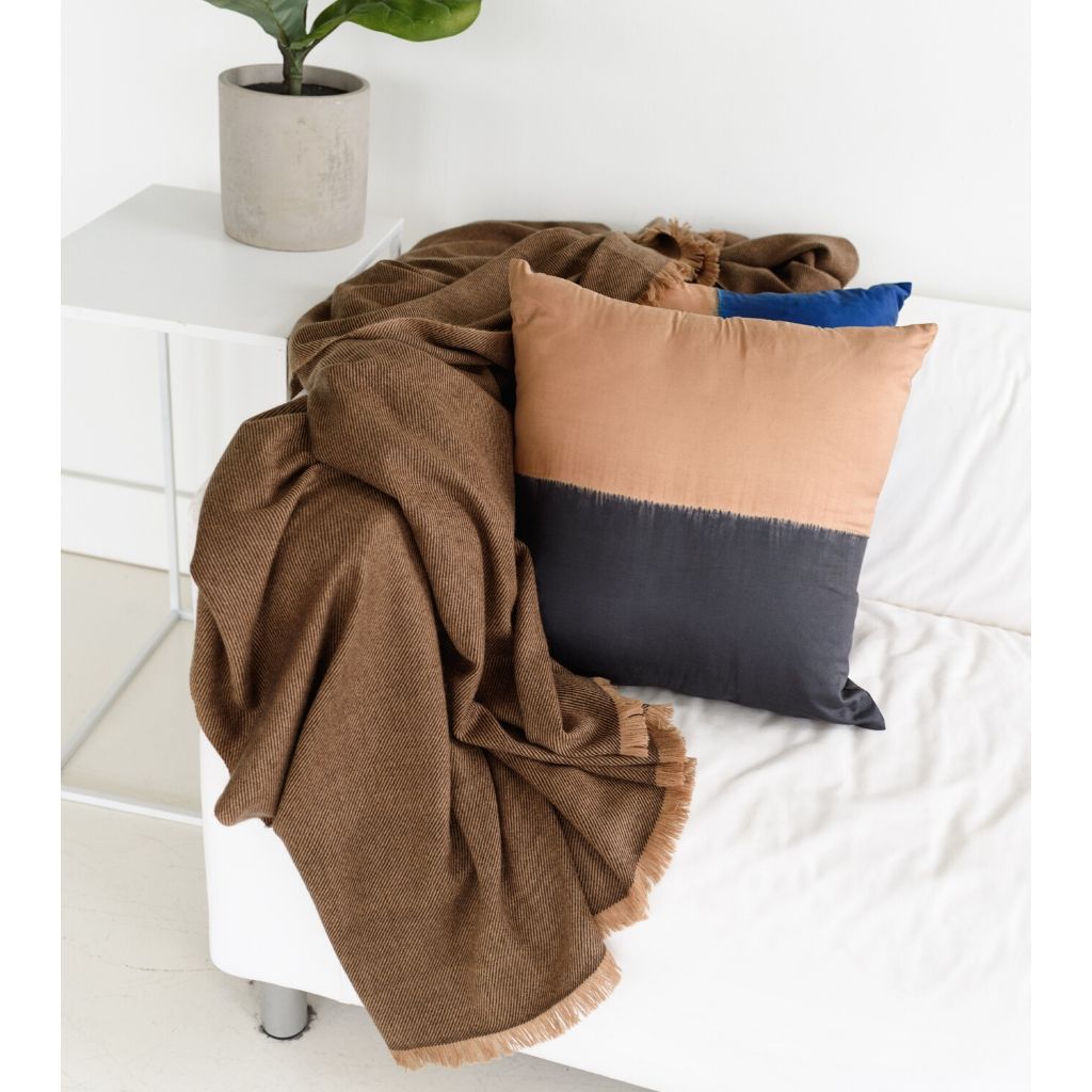 Kala Black &amp; Gold Color Block Mulberry Silk Square Pillow with a cozy blanket on a modern sofa.
