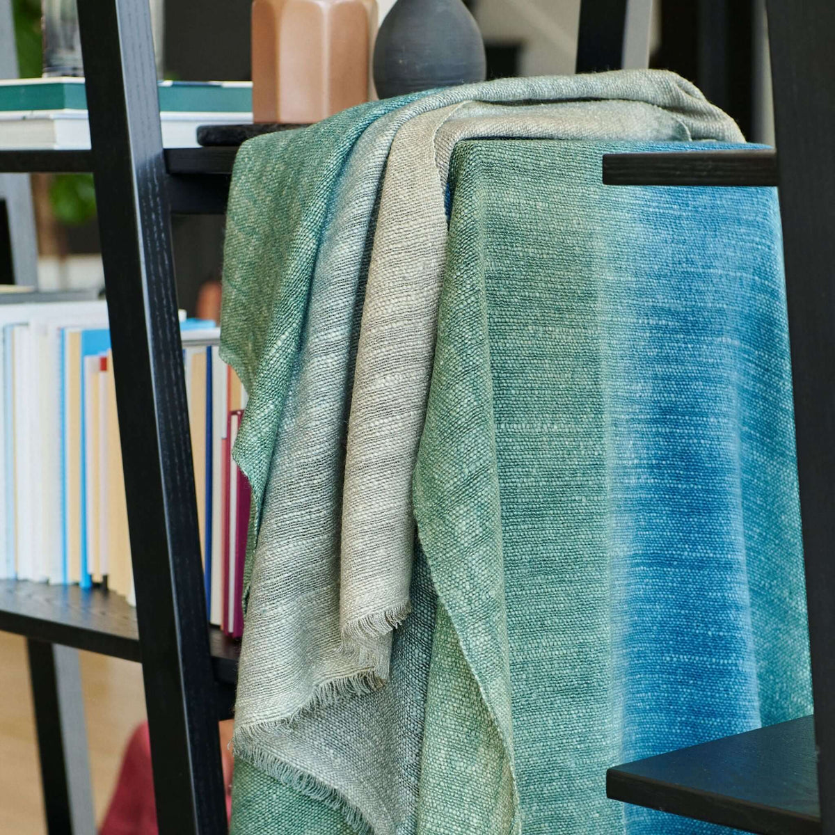 Lake Moss Handwoven Merino Throw Blanket draped over a shelf, showcasing serene blue and green shades.