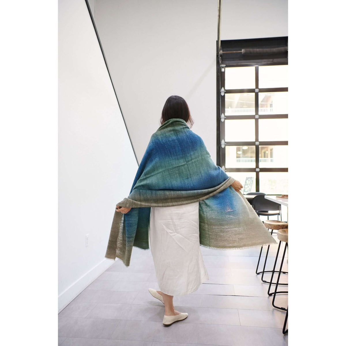 Woman wearing a Lake Moss handwoven merino throw blanket showcasing serene shades of blue green.