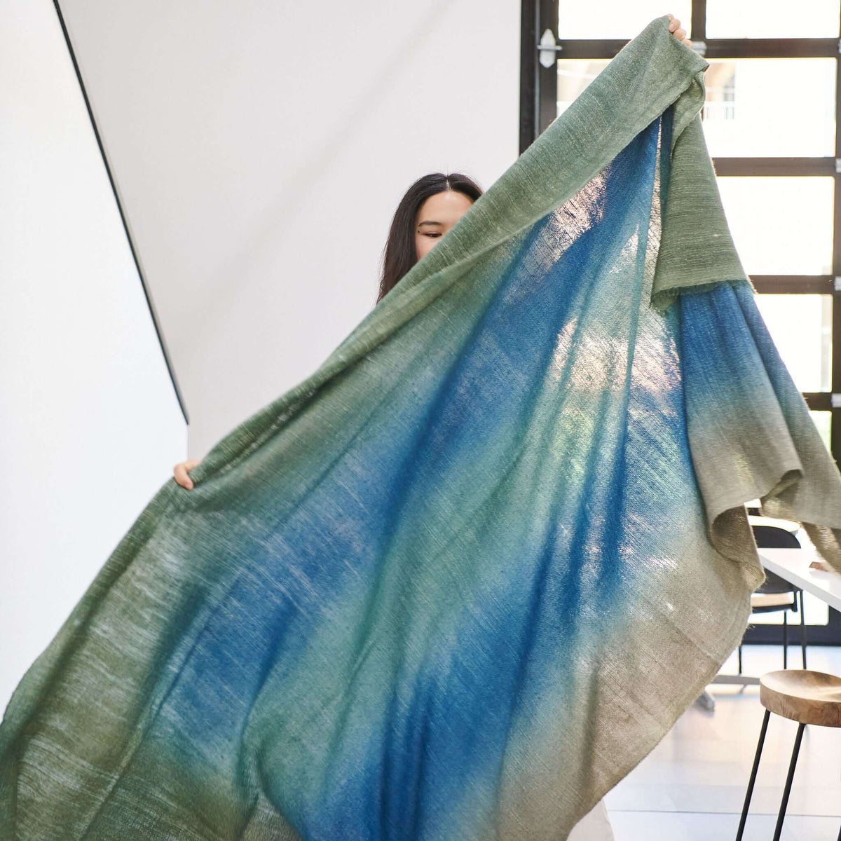 A woman holding the Lake Moss Handwoven Merino Throw Blanket, showcasing serene blue-green shades.