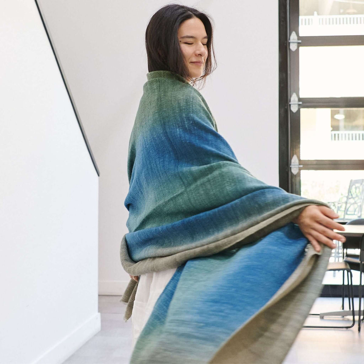 Model draped in Lake Moss handwoven merino throw blanket showcasing serene shades of blue and green.