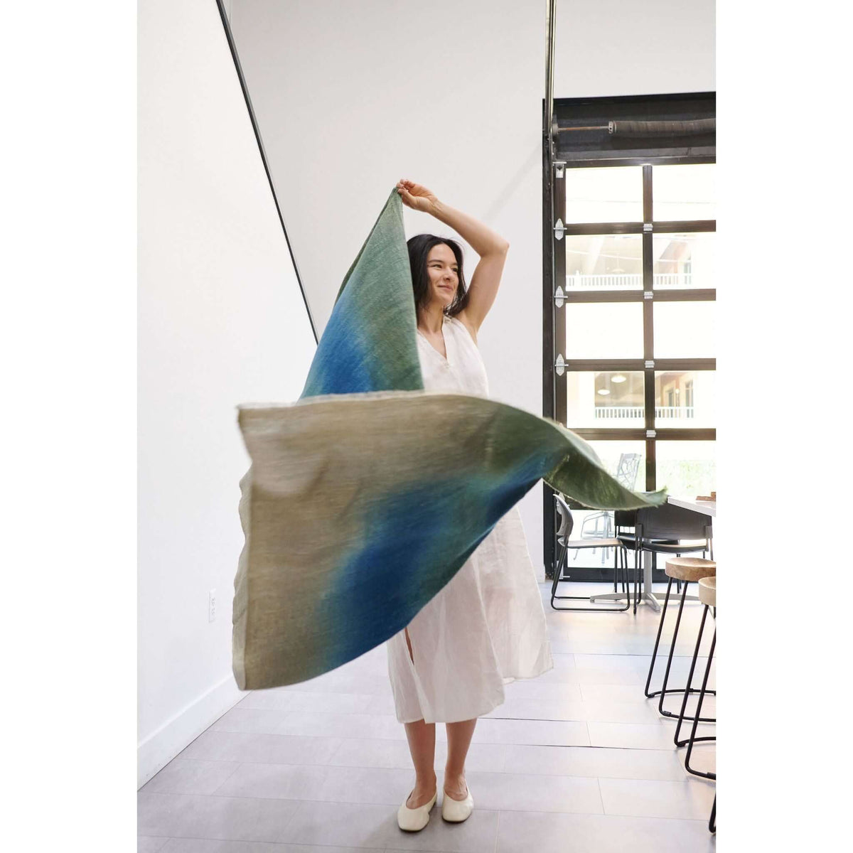 Woman elegantly showcasing the Lake Moss handwoven merino throw blanket in serene shades of blue and green.