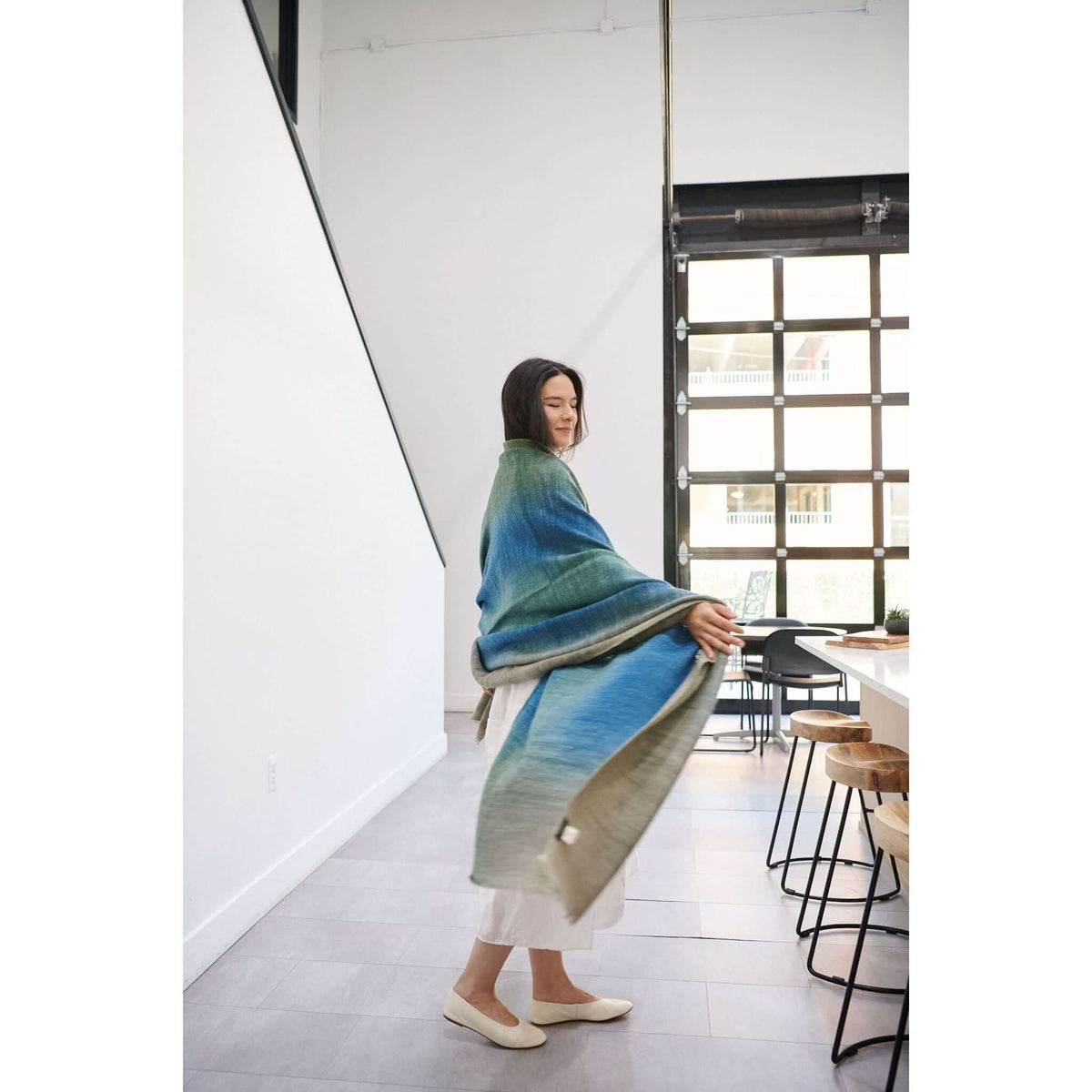 Model displaying the Lake Moss handwoven merino throw blanket in serene shades of blue and green, showcasing its softness.