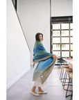 Model displaying the Lake Moss handwoven merino throw blanket in serene shades of blue and green, showcasing its softness.