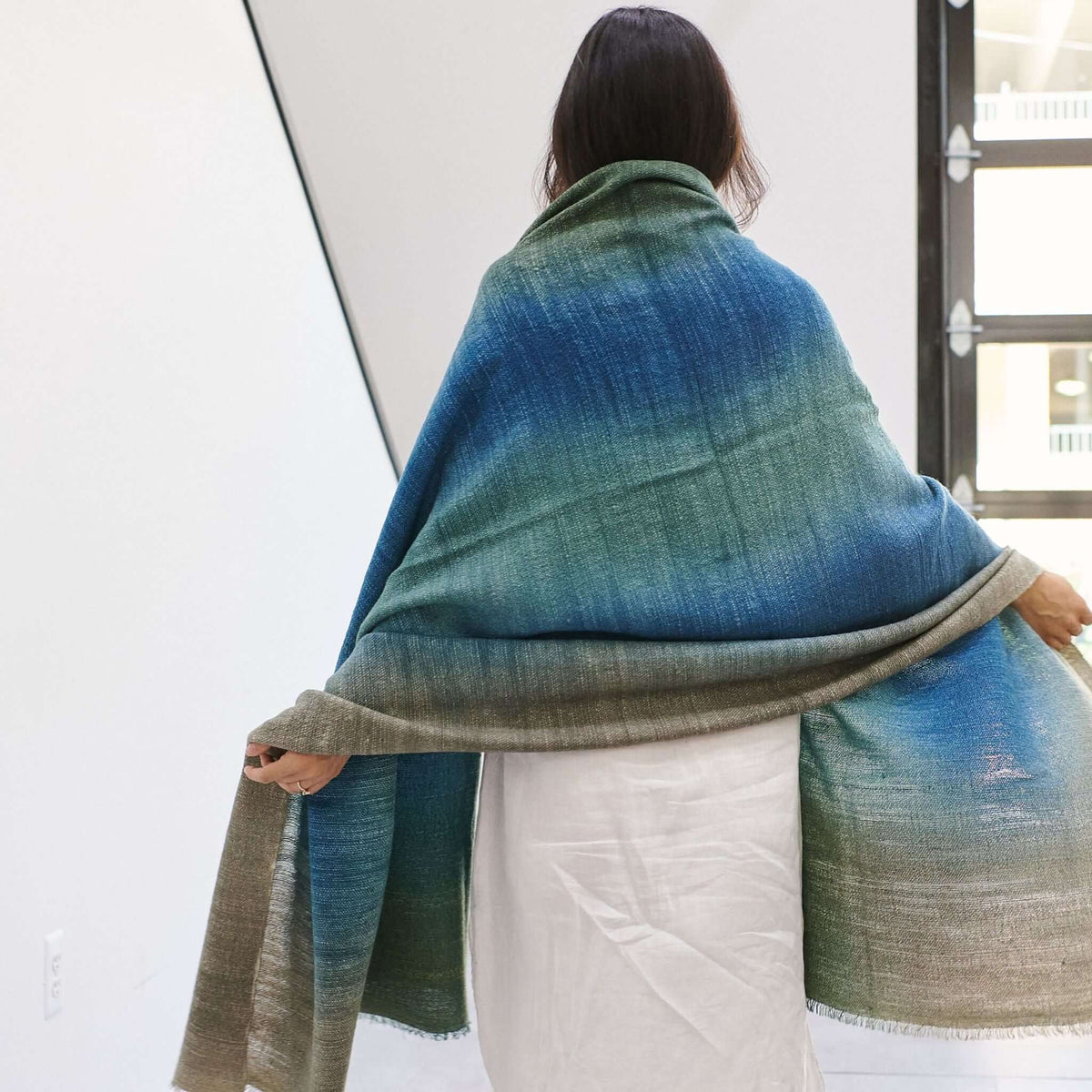 Woman draped in Lake Moss handwoven merino throw blanket, showcasing serene blue-green hues and artisan quality.