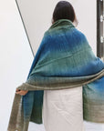 Woman draped in Lake Moss handwoven merino throw blanket, showcasing serene blue-green hues and artisan quality.