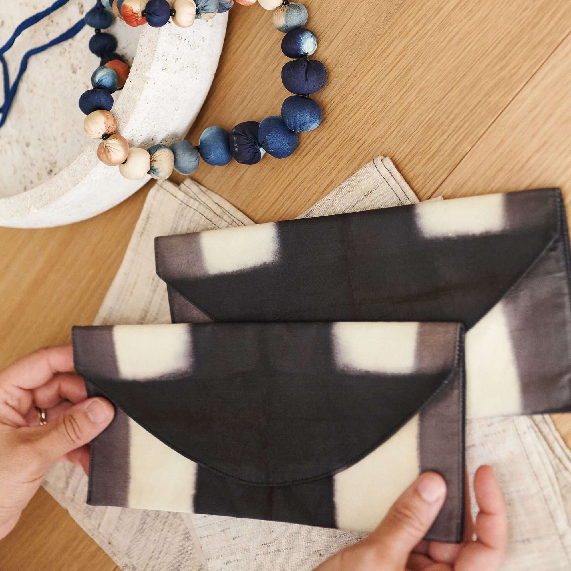 Melo Black Handcrafted Silk Travel Pouch Organizer displayed on wooden surface with hands holding two pouches.