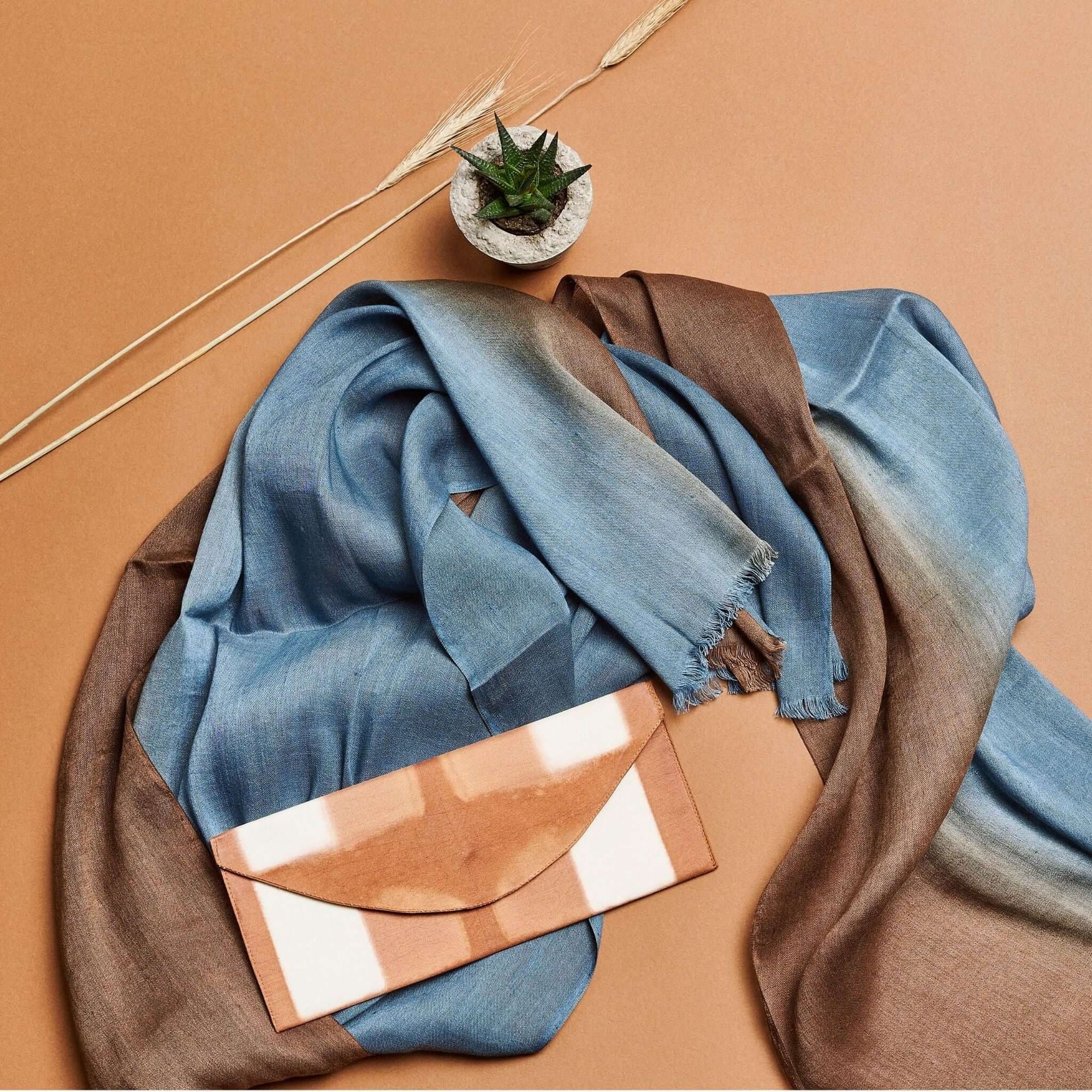 Melo Gold Mulberry Silk Shibori Hand Crafted Envelope Pouch on a blue and brown scarf with a plant.