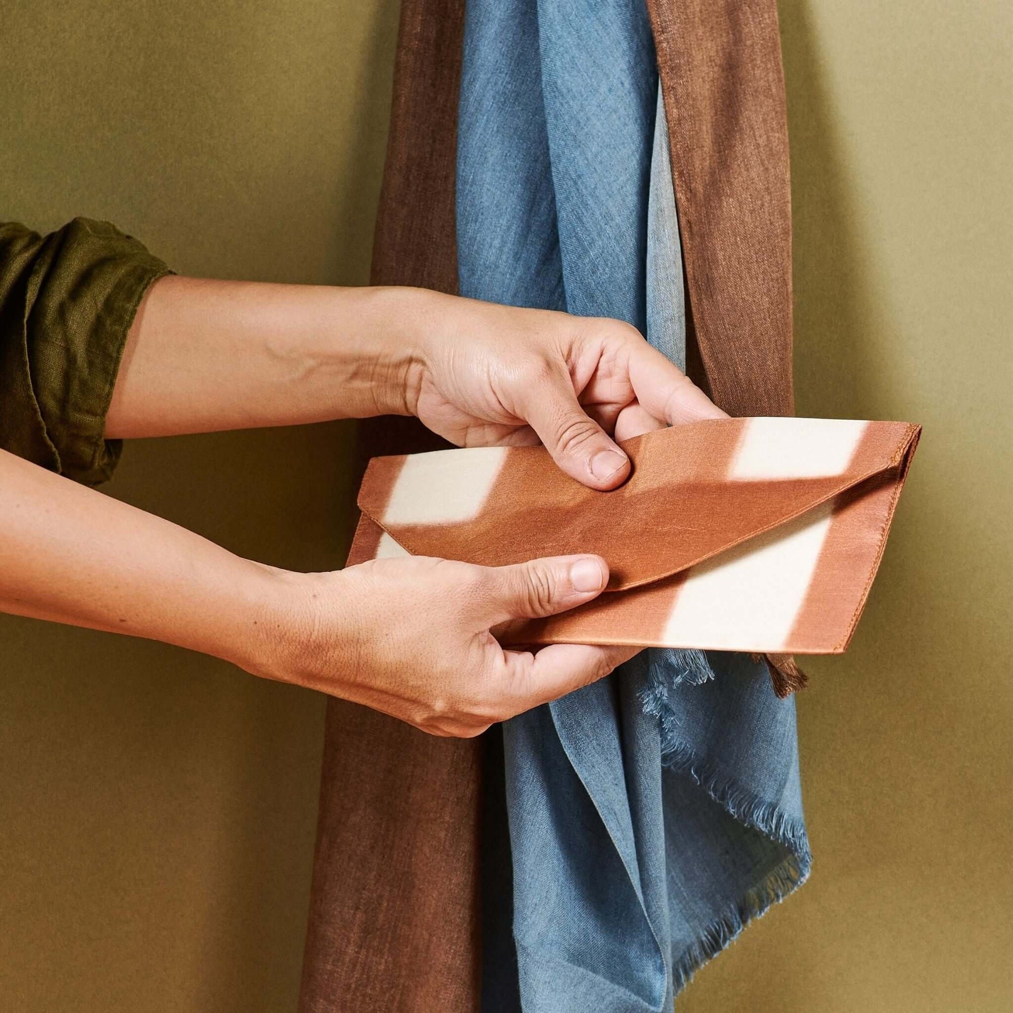 Person holding the Melo Gold Mulberry Silk Shibori Hand Crafted Envelope Pouch with a soft fabric backdrop.