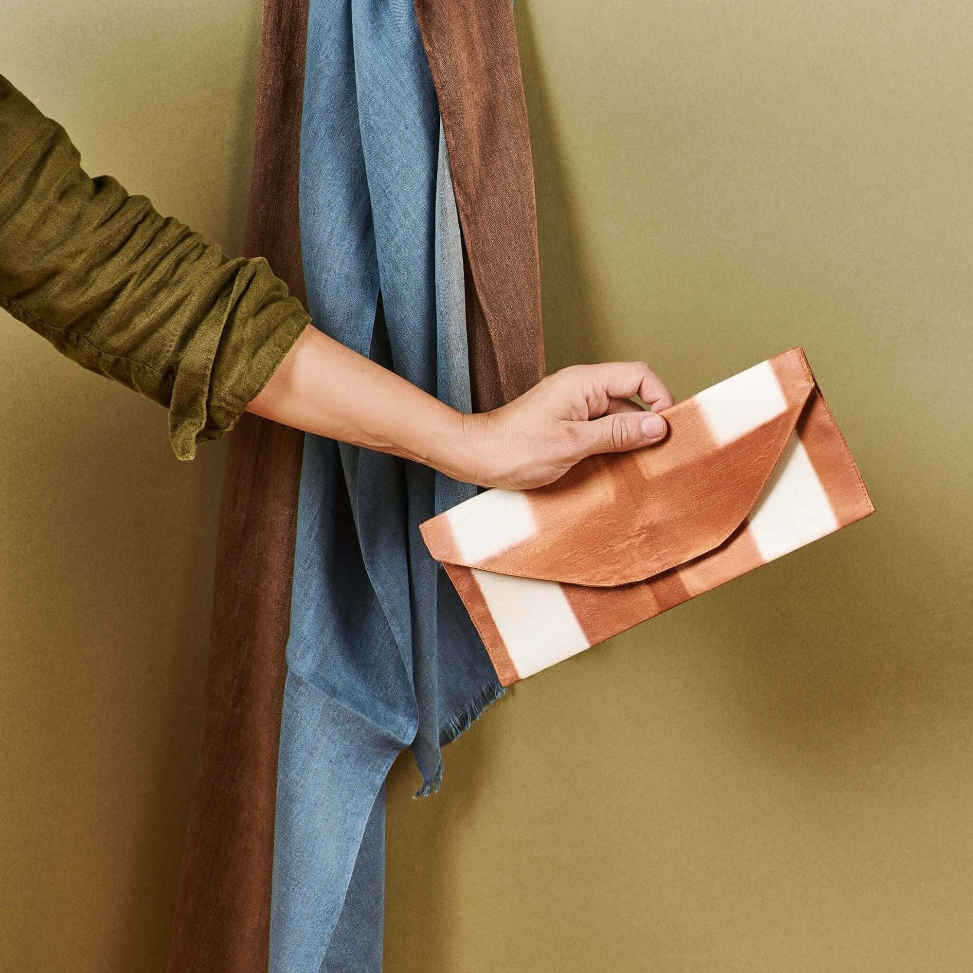 Person holding Melo Gold Mulberry Silk Shibori Hand Crafted Envelope Pouch against a green background.