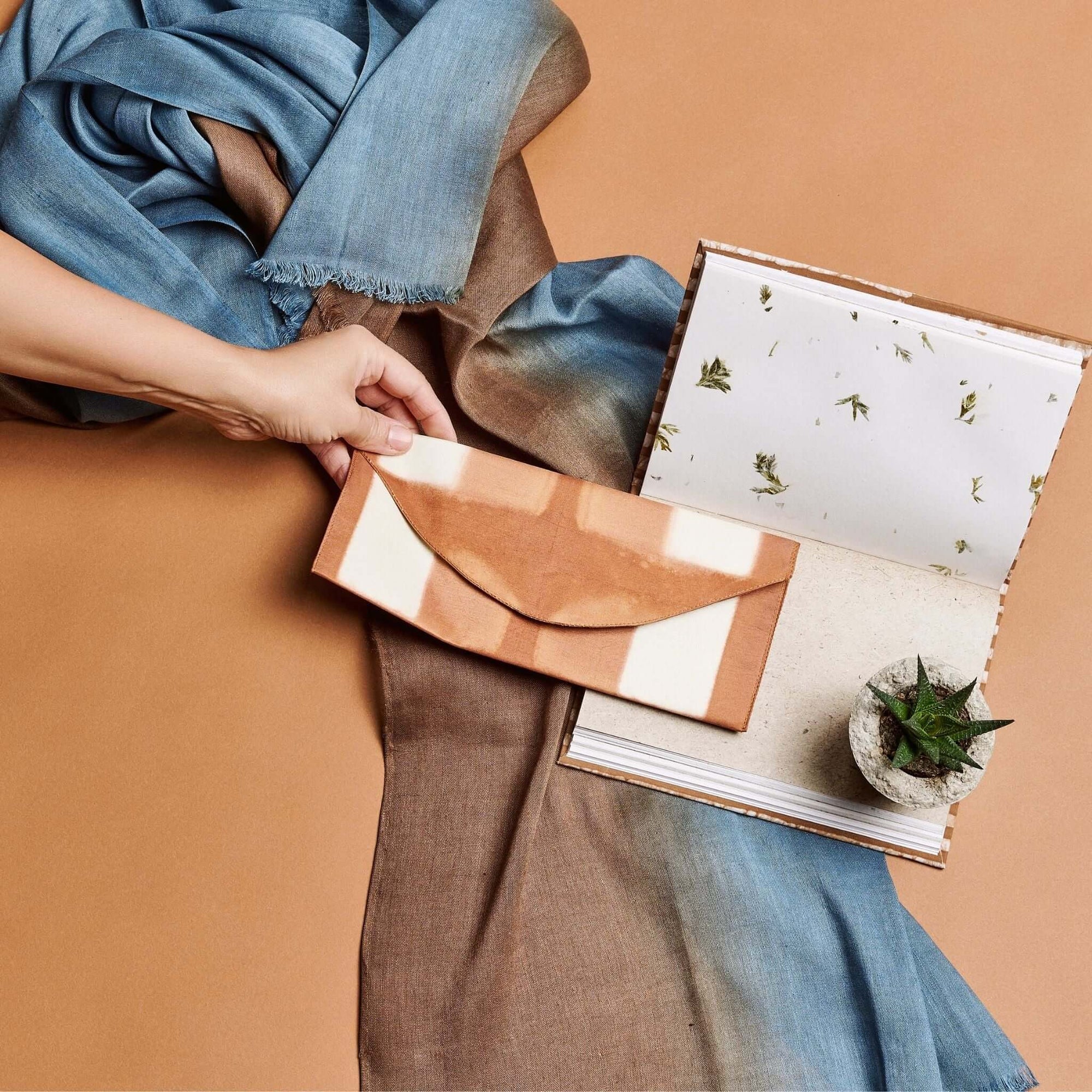 Melo Gold Mulberry Silk Shibori Hand Crafted Envelope Pouch held with a scarf and a notebook in the background.