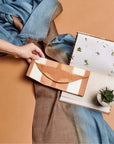 Melo Gold Mulberry Silk Shibori Hand Crafted Envelope Pouch held with a scarf and a notebook in the background.