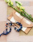 Mihika silk beaded necklace displayed with a chic envelope and flowers on a textured background.