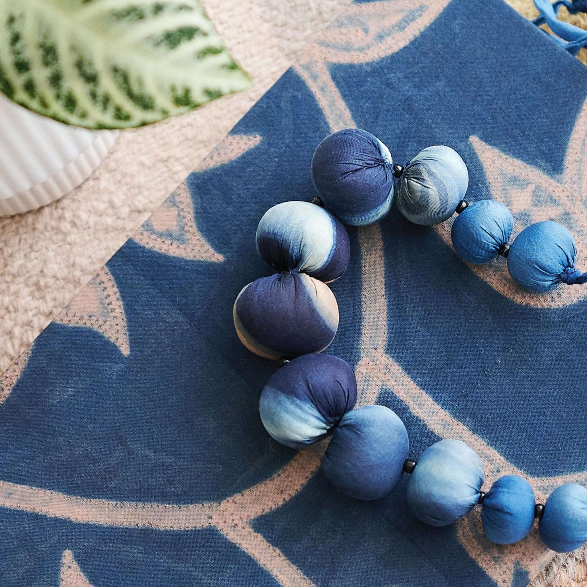 Mihika silk beaded necklace showcasing handcrafted blue silk beads on a textile background.