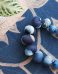 Mihika silk beaded necklace showcasing handcrafted blue silk beads on a textile background.