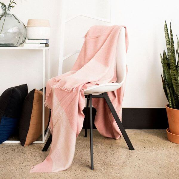 Rosa Plush Maroon Plush Merino Queen Bedspread / Large Throw draped over a chair, showcasing its soft colors and fringes.