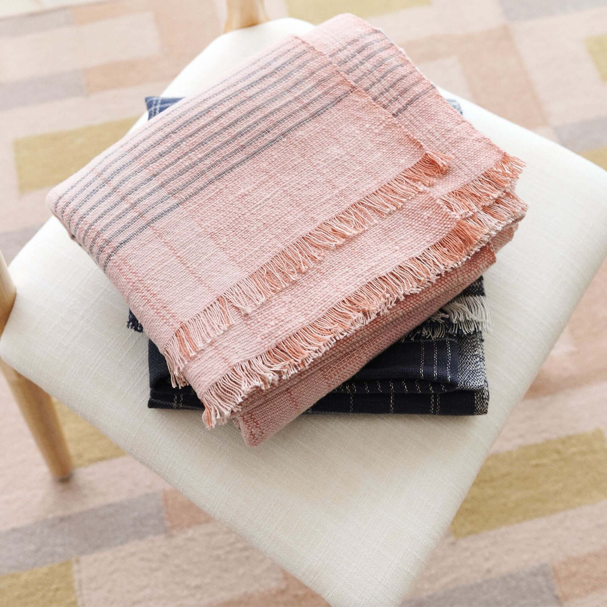 Silica Rose In Shades of Salmon Pink Gray Stripes Pattern Soft Handwoven Merino Throw neatly folded on a chair.