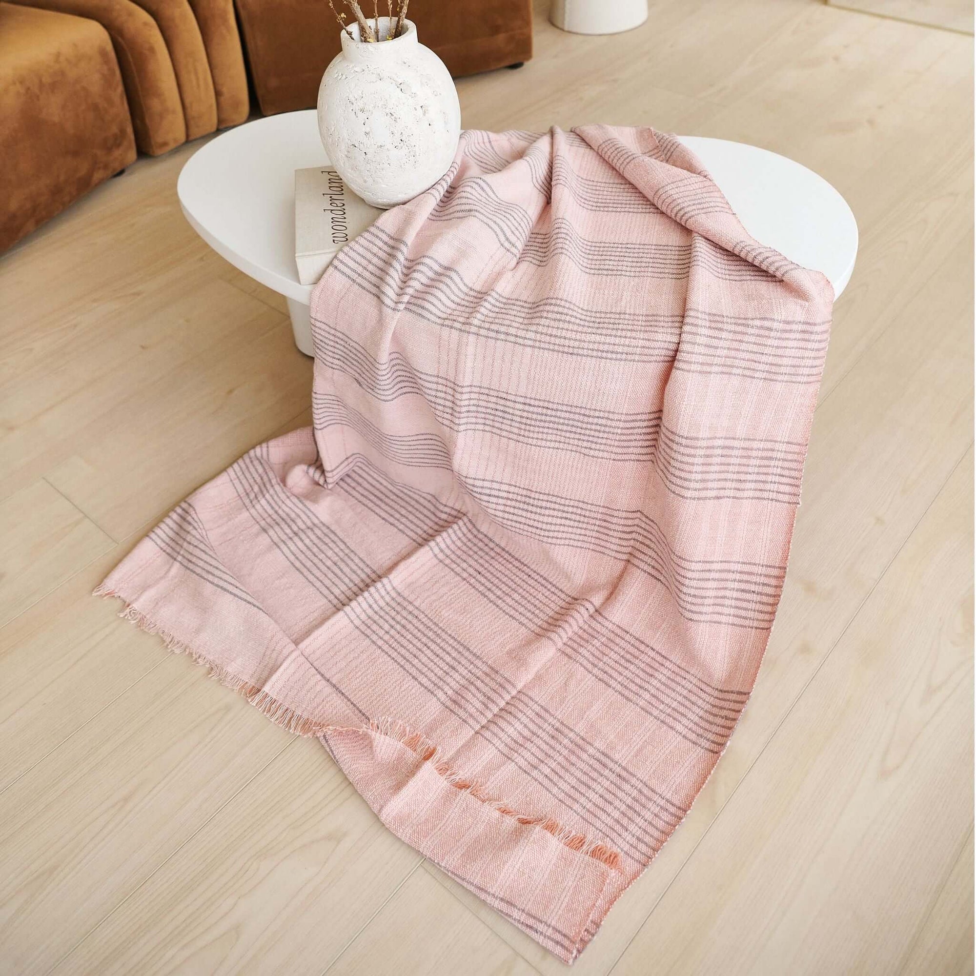 Silica Rose In Shades of Salmon Pink Gray Stripes Pattern Soft Handwoven Merino Throw draped on a modern coffee table.