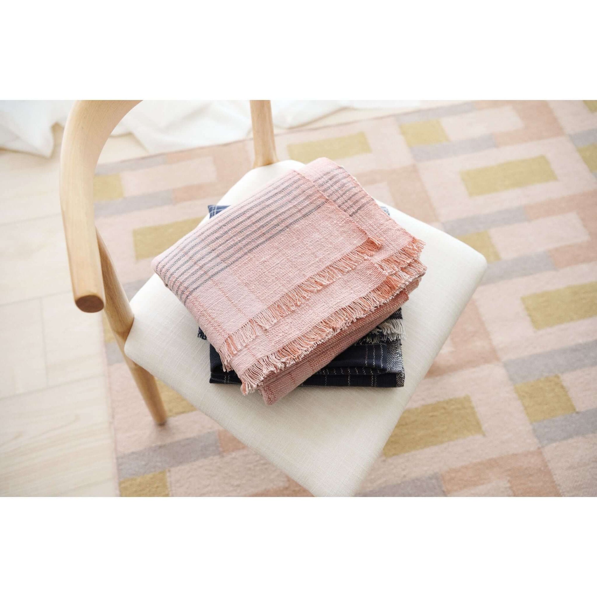 Silica Rose In Shades of Salmon Pink Gray Stripes Pattern Soft Handwoven Merino Throw draped on a chair.