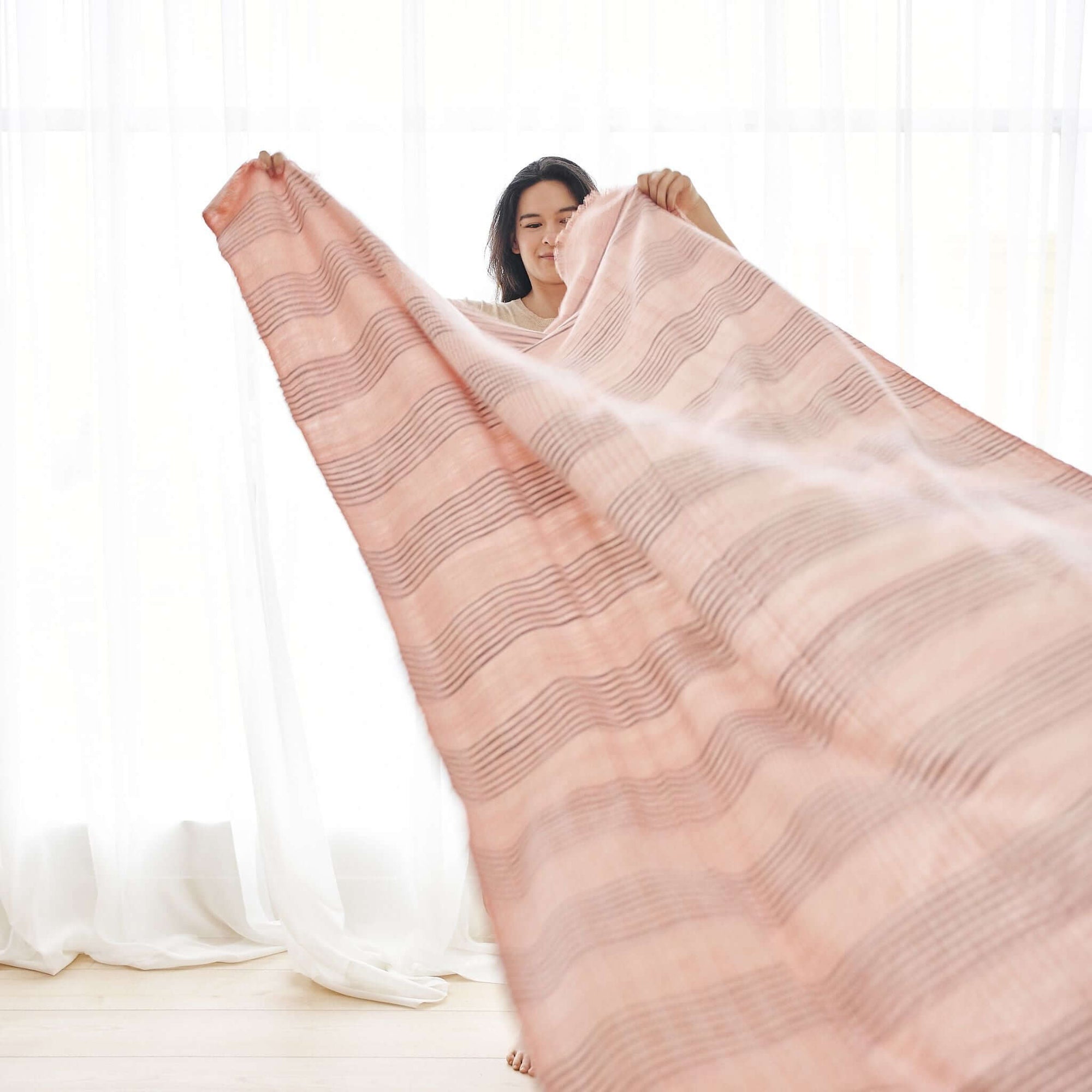 Silica Rose In Shades of Salmon Pink Gray Stripes Pattern Soft Handwoven Merino Throw displayed by a model indoors.
