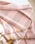 Silica Rose In Shades of Salmon Pink Gray Stripes Pattern Soft Handwoven Merino Throw draped over a table.