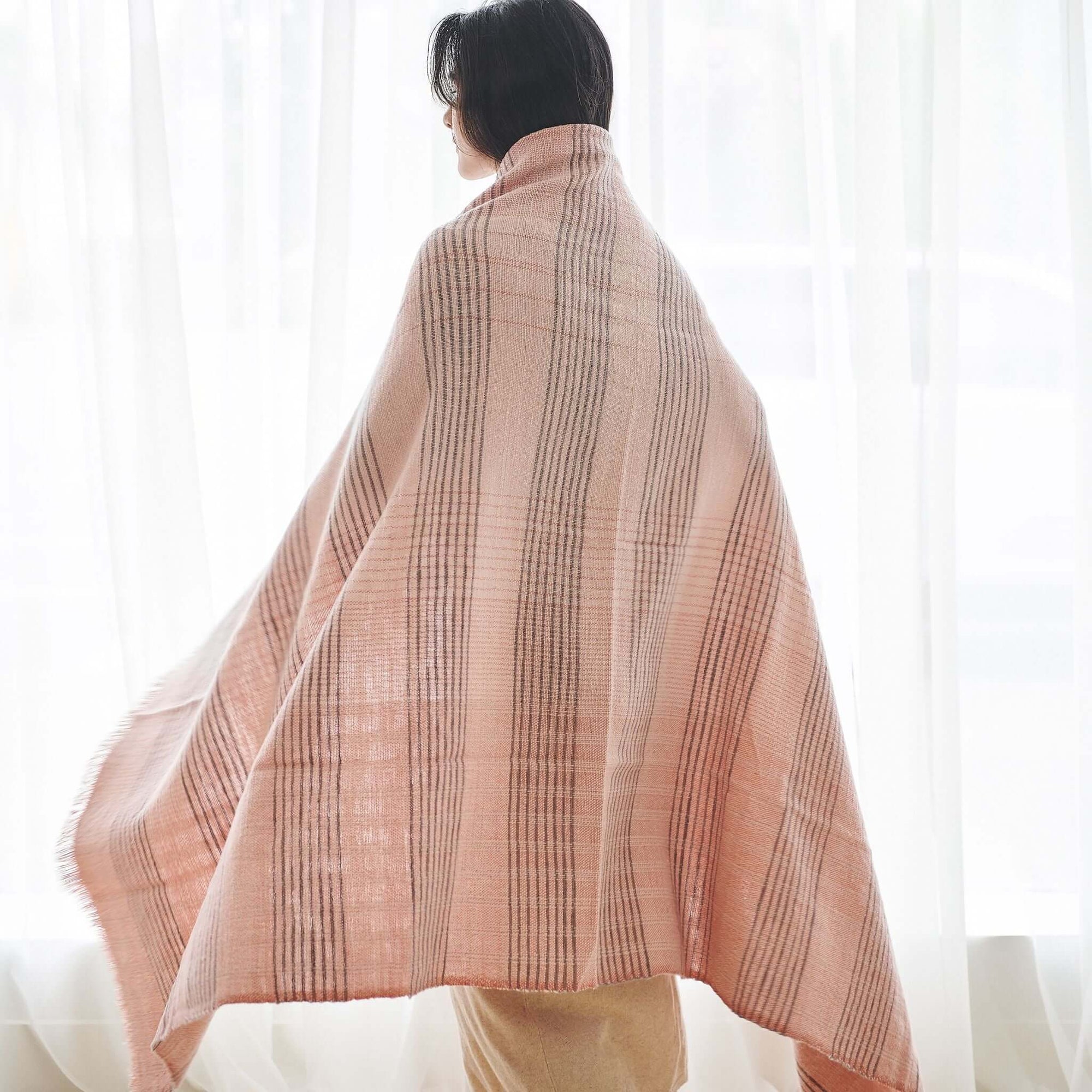 Silica Rose In Shades of Salmon Pink Gray Stripes Pattern Soft Handwoven Merino Throw draped over a model.