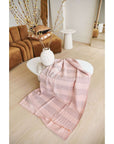 Silica Rose In Shades of Salmon Pink Gray Stripes Pattern Soft Handwoven Merino Throw draped on a modern coffee table.