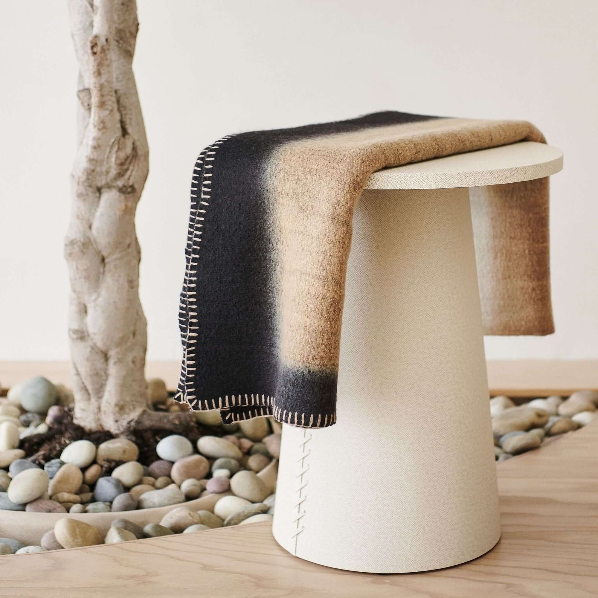 Siro Brown Handwoven Merino Artisan Throw Blanket draped over a modern white stool in a minimalist setting.