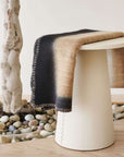 Siro Brown Handwoven Merino Artisan Throw Blanket draped over a modern white stool in a minimalist setting.