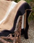 Siro Brown Handwoven Merino Artisan Throw Blanket draped over a rustic chair, highlighting the intricate stitching and rich colors.