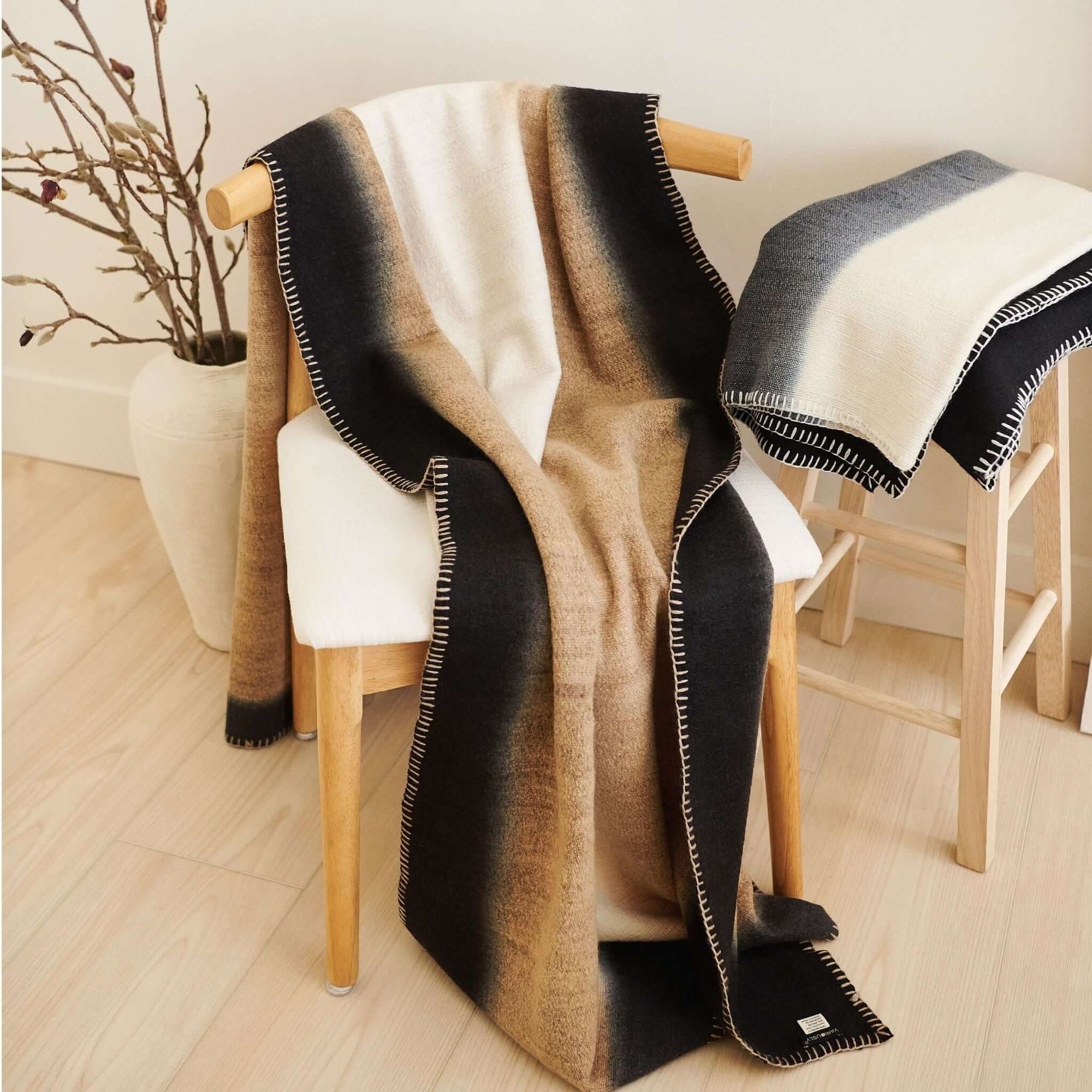 Siro Brown Handwoven Merino Artisan Throw Blanket draped over a chair, showcasing its soft textures and elegant design.