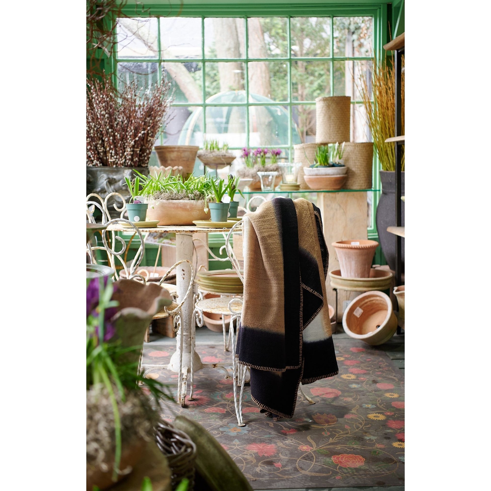 Siro Brown Handwoven Merino Artisan Throw Blanket draped over a chair in a beautifully arranged green indoor garden.