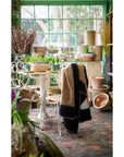 Siro Brown Handwoven Merino Artisan Throw Blanket draped over a chair in a beautifully arranged green indoor garden.