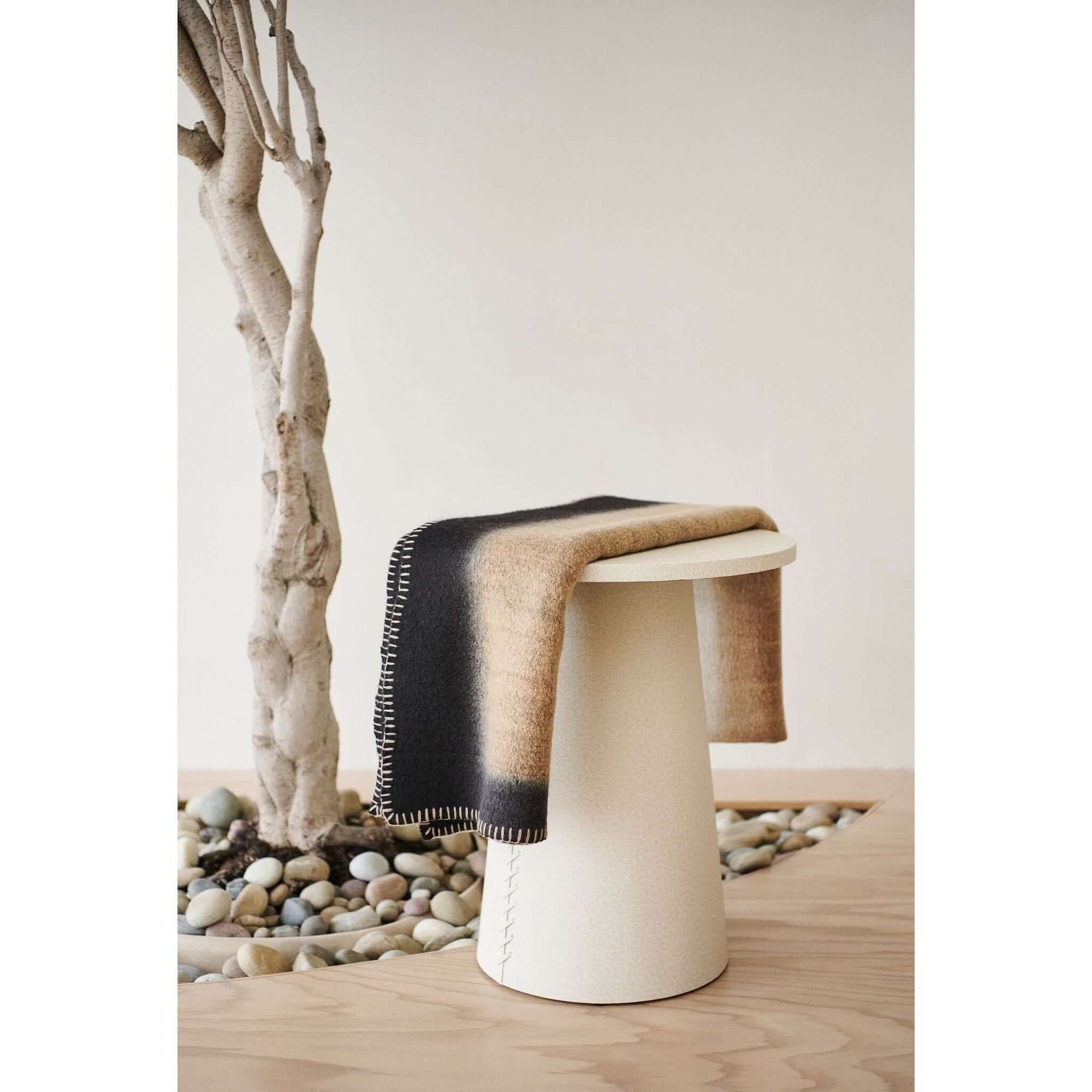 Siro Brown Handwoven Merino Artisan Throw Blanket elegantly draped over a modern stool, showcasing its stylish design.