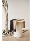 Siro Brown Handwoven Merino Artisan Throw Blanket elegantly draped over a modern stool, showcasing its stylish design.