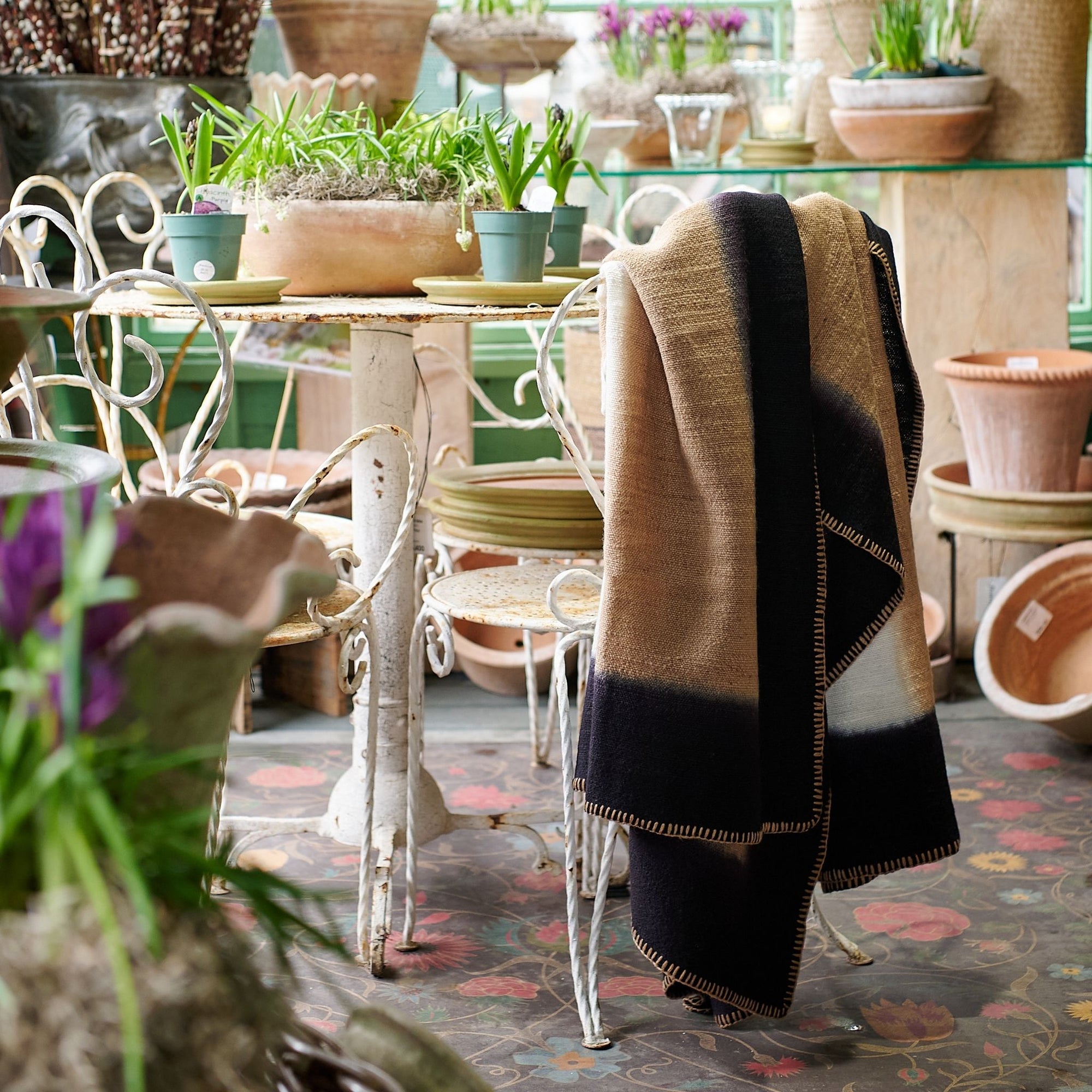 Siro Brown Handwoven Merino Artisan Throw Blanket displayed on a chair in a cozy plant-filled setting.
