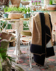 Siro Brown Handwoven Merino Artisan Throw Blanket displayed on a chair in a cozy plant-filled setting.