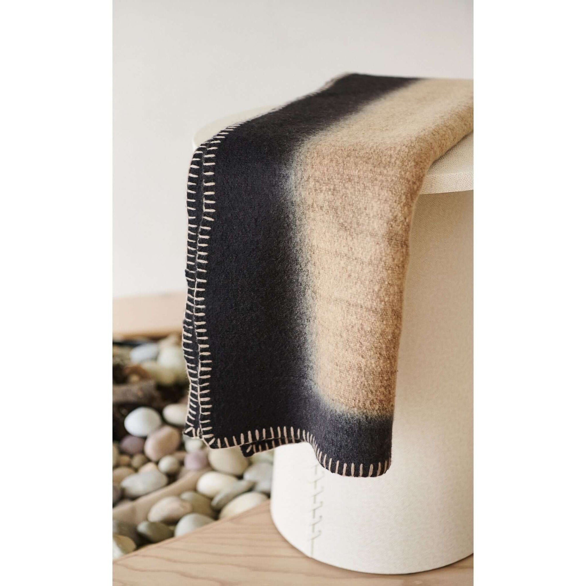Siro Brown Handwoven Merino Artisan Throw Blanket draped elegantly on a modern stool, showcasing its unique texture and color.