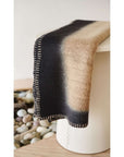 Siro Brown Handwoven Merino Artisan Throw Blanket draped elegantly on a modern stool, showcasing its unique texture and color.