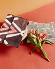 Tisa Artisanal Pouch In Black Pink Triangle Print displayed with geometric patterned pouches and a flower.