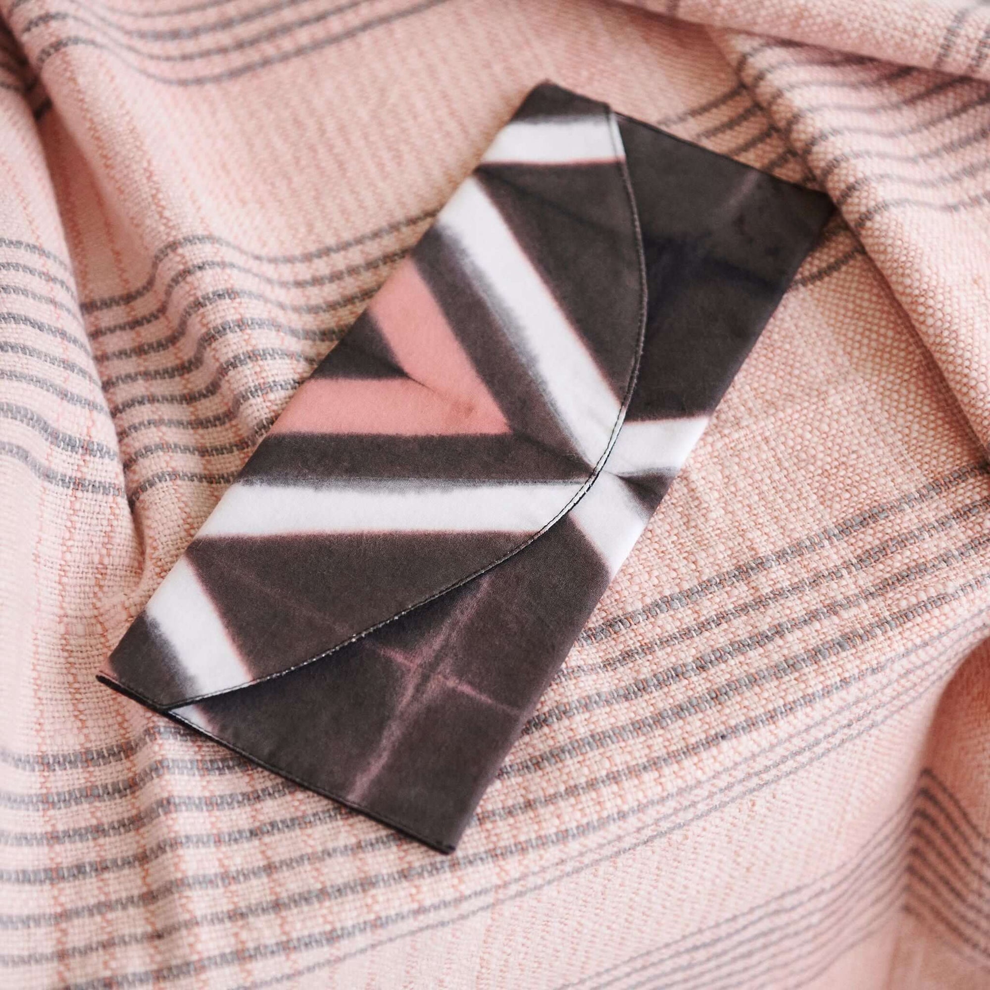 Tisa Artisanal Pouch In Black Pink Triangle Print displayed on a soft, pink patterned fabric backdrop.
