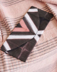 Tisa Artisanal Pouch In Black Pink Triangle Print displayed on a soft, pink patterned fabric backdrop.