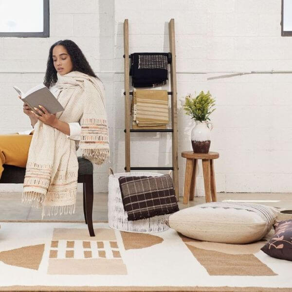 Unah Coral Hand Embroidered Handwoven Cotton Artisan Throw draped over a woman reading in a cozy indoor setting.