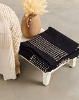 Walnut Black Yak With Hand Knotted Merino Stripes Handloom Throw displayed on a wooden table with a decorative vase.