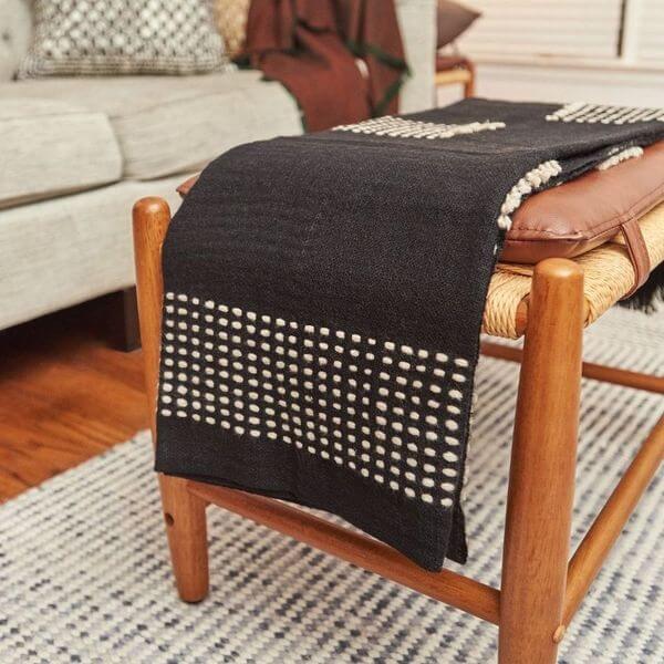 Walnut Black Yak With Hand Knotted Merino Stripes Handloom Throw draped over a wooden stool in a cozy living room.