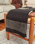 Walnut Black Yak With Hand Knotted Merino Stripes Handloom Throw draped over a wooden stool in a cozy living room.